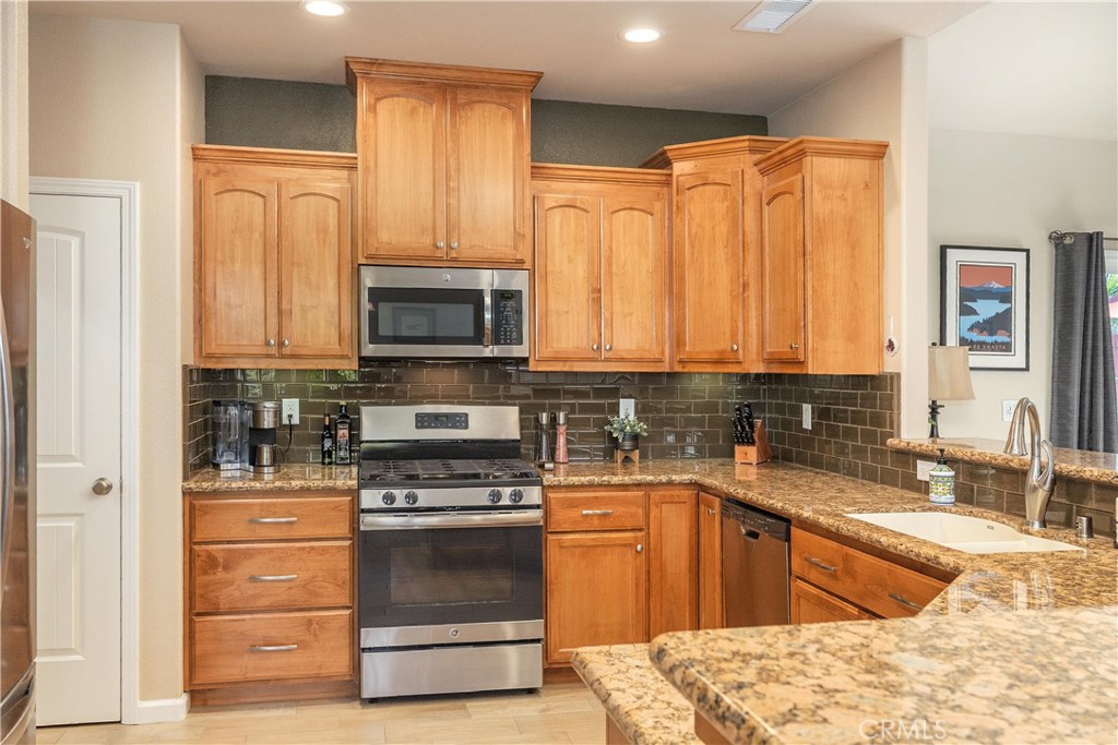 Kitchen with warm wood cabinets, granite counters, dark tile backsplash, and stainless steel appliances.