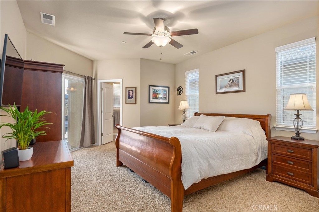 Furnished bedroom with a wooden sleigh bed, white bedding, ceiling fan, and carpet.