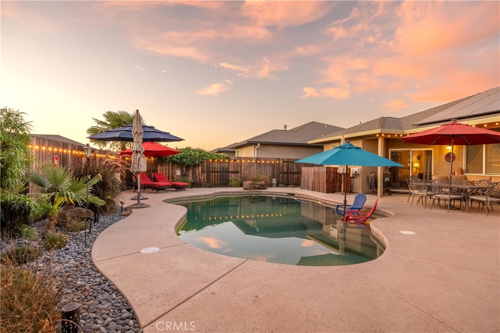Backyard pool and curved patio with colorful umbrellas and outdoor seating at sunset.