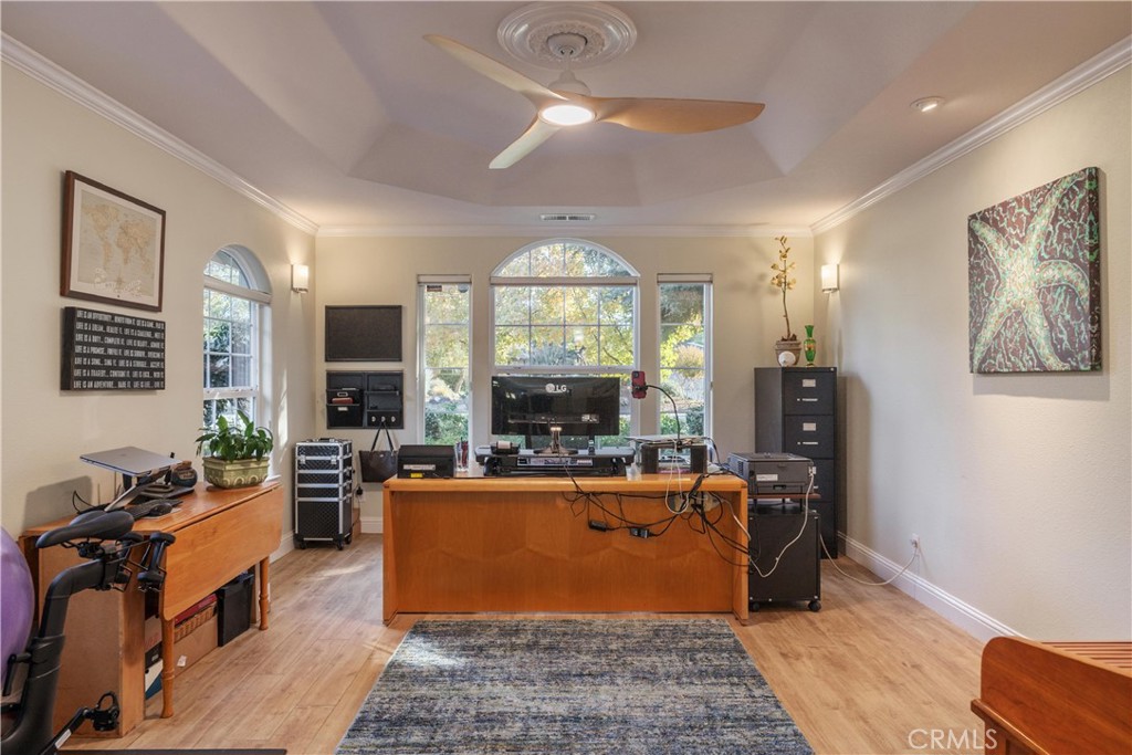 Furnished home office with arched windows, wooden desks, and computer equipment.