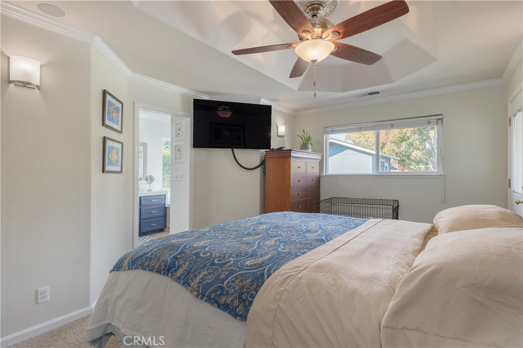 Bedroom with a blue patterned throw, ceiling fan, wall-mounted television, and large window.