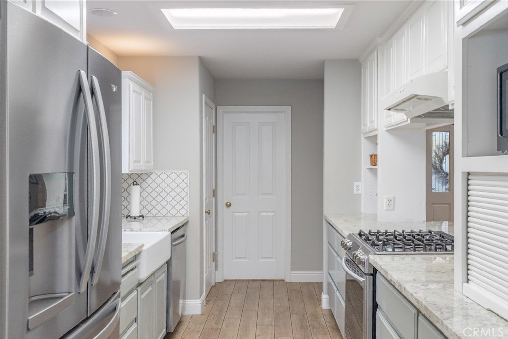Narrow kitchen with white cabinets, farmhouse sink, stainless refrigerator, and gas range.