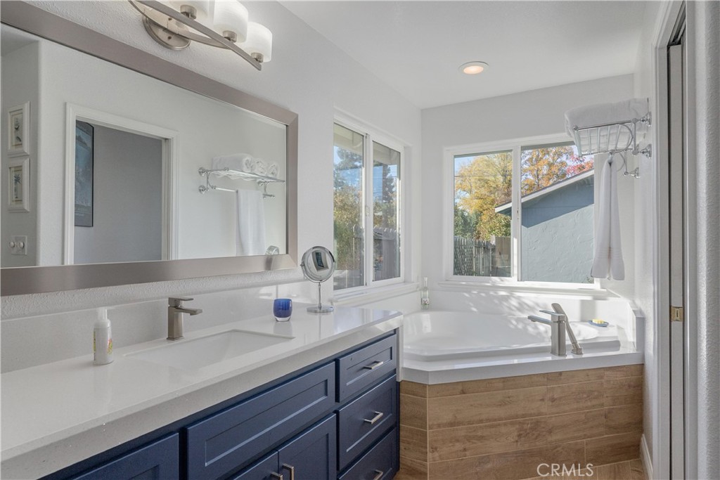 Bathroom with a dark blue vanity and corner soaking tub beneath large windows.