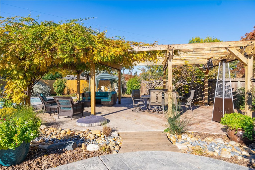 Backyard patio beneath a vine-covered wooden pergola, with outdoor seating and a patio heater.