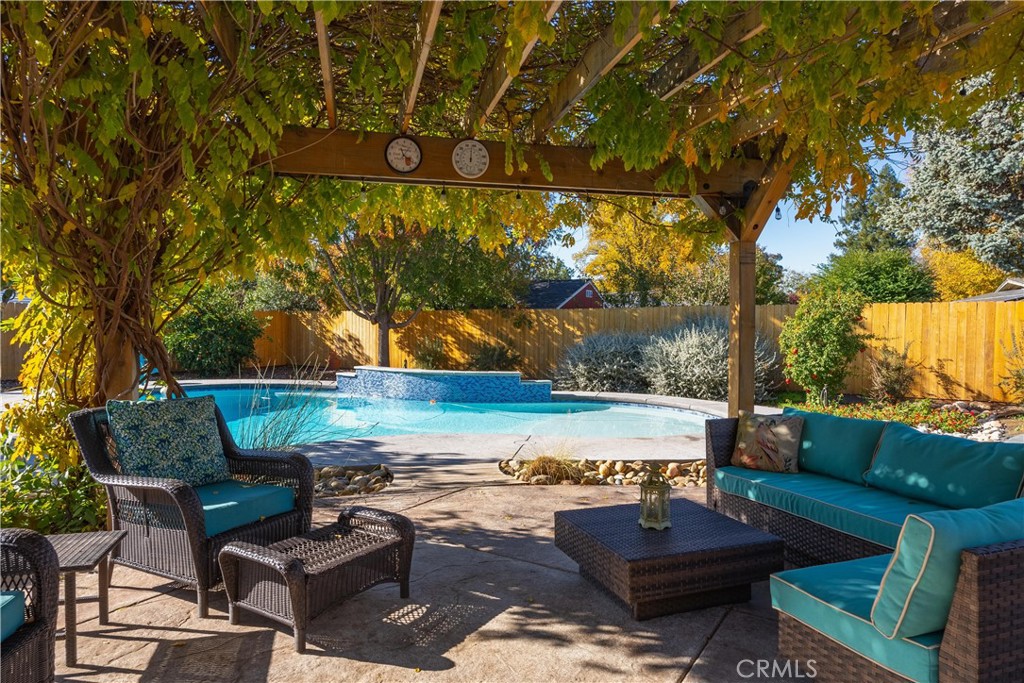 Backyard pool and stone patio with teal wicker seating beneath an autumn-covered pergola.