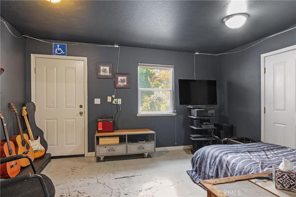 Bedroom with gray walls, guitars, a television, and an accessible sign above the door.