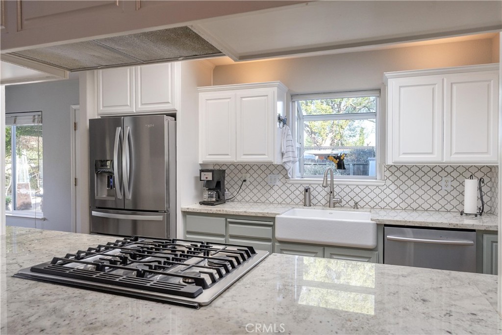 Kitchen with a farmhouse sink, patterned tile backsplash, and gas cooktop set into a broad stone island.