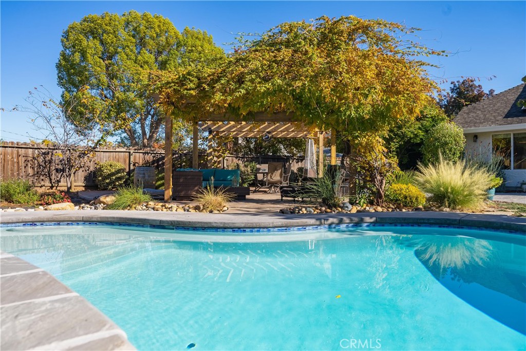 Backyard pool beside a vine-covered pergola with outdoor seating and autumn foliage.