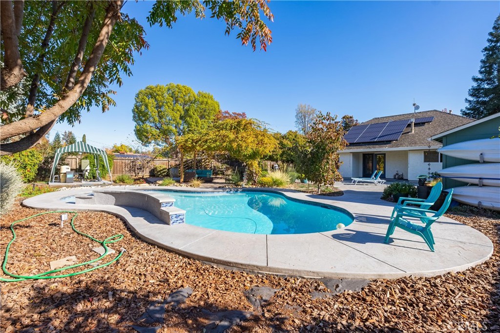 Backyard swimming pool with a curved shape, concrete patio, turquoise chairs, and rooftop solar panels.