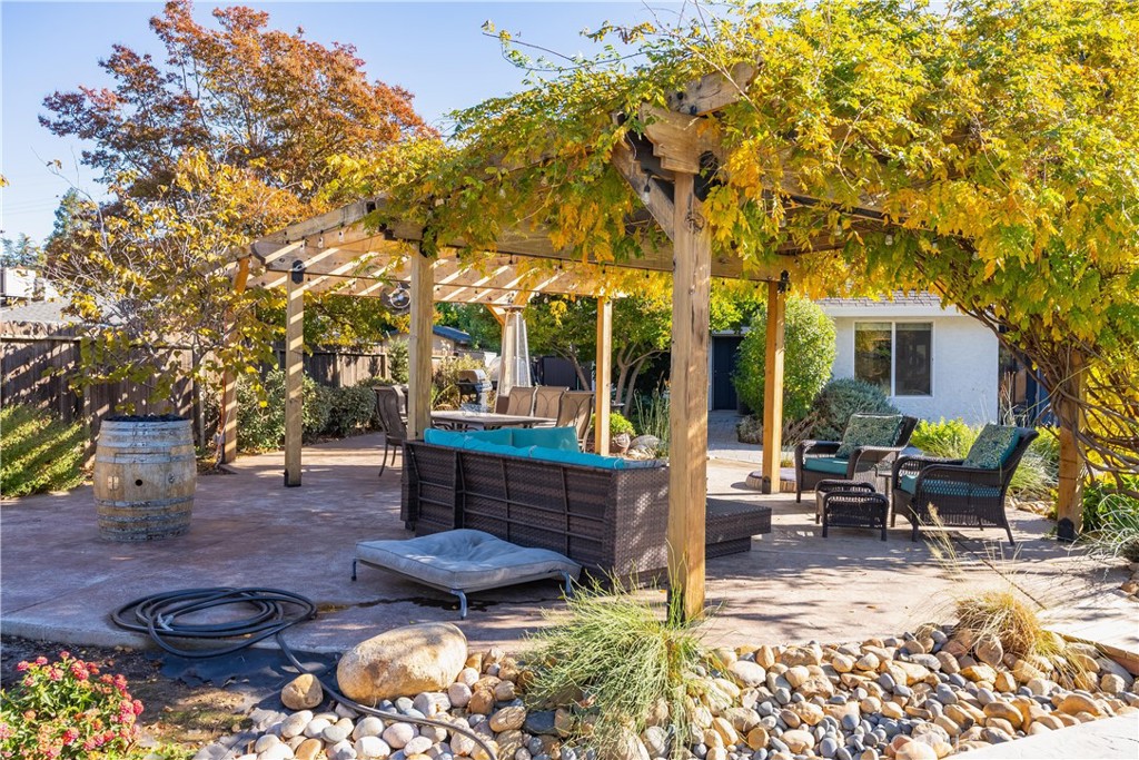 Backyard patio with lounge seating beneath a vine-covered wooden pergola.
