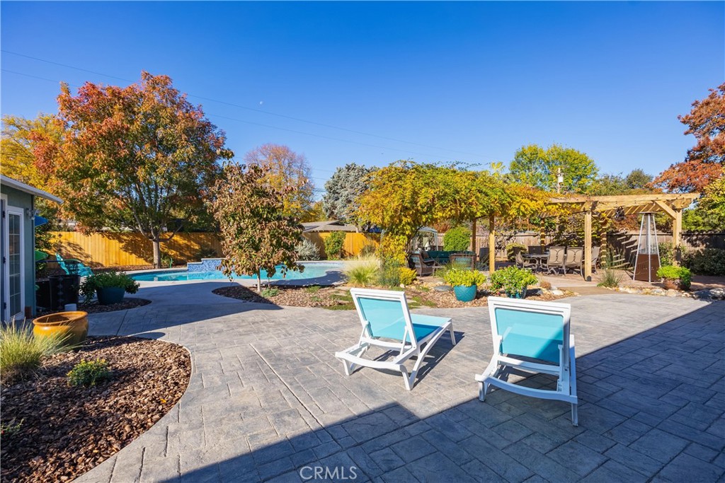 Backyard pool and paved patio with blue lounge chairs and a pergola.