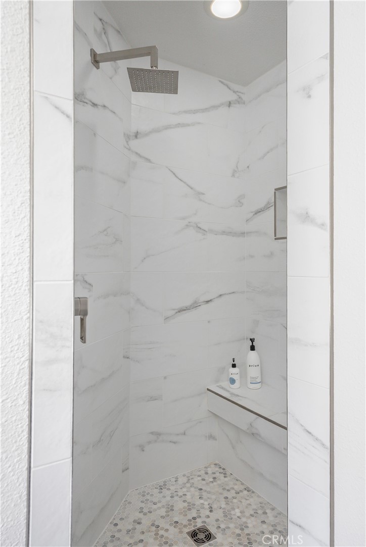 Walk-in shower with marble-look tile, a square rainfall showerhead, built-in bench, and mosaic floor.