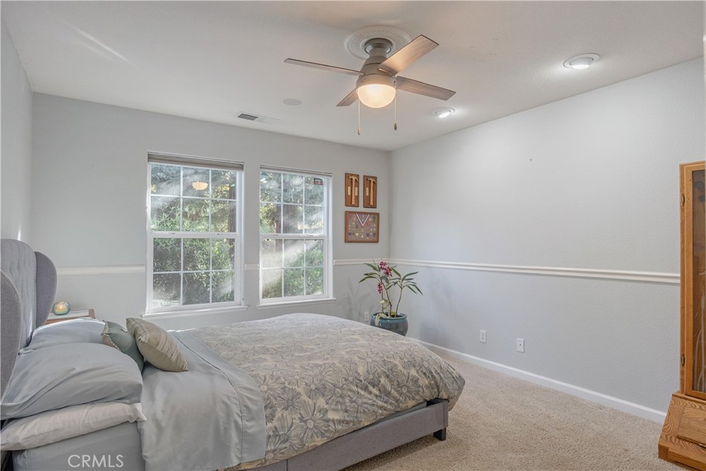 Furnished bedroom with a floral comforter, two windows, and a ceiling fan.