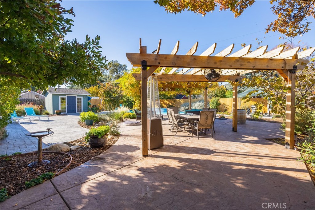 Backyard patio with a wooden pergola, outdoor dining table, paved seating areas, and landscaped garden.