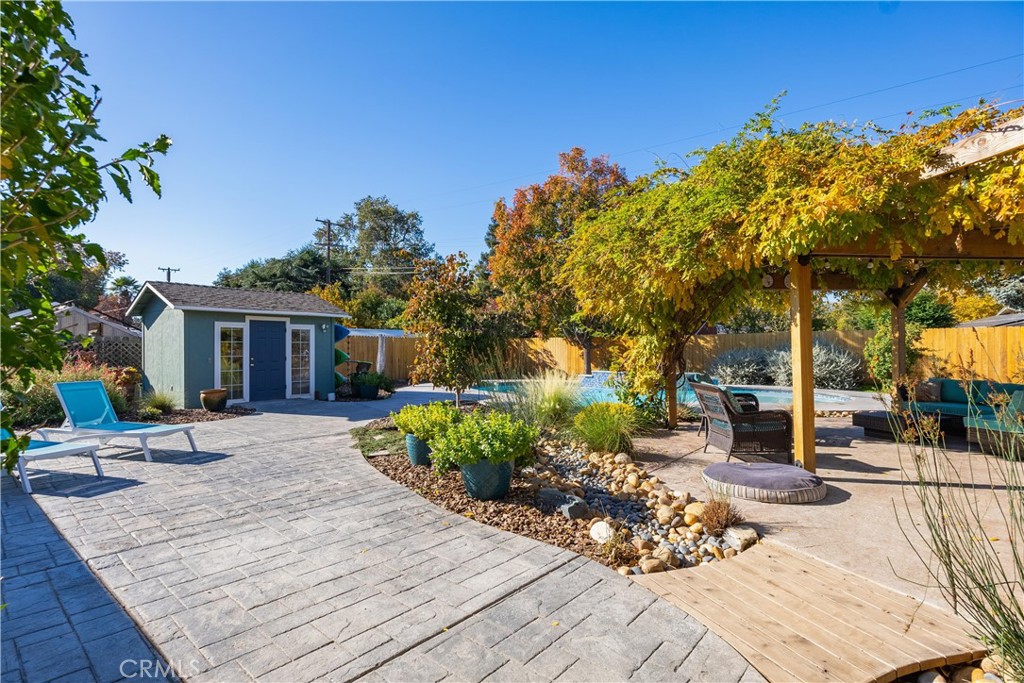 Backyard patio and pool with vine-covered pergola, outdoor seating, and a small shed.