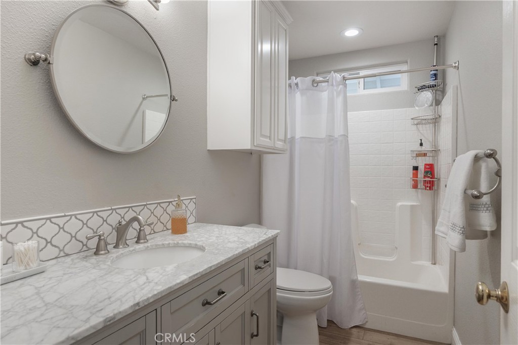 Bathroom with a marble-look vanity and mirror beside a white walk-in tub and shower curtain.