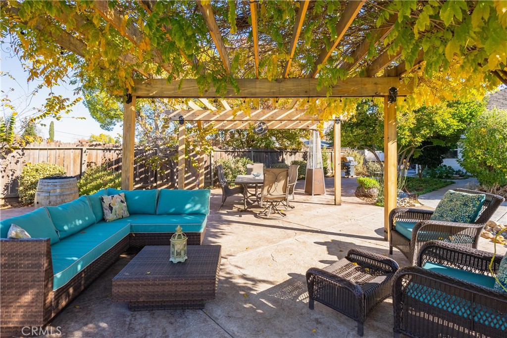 Backyard patio with a leafy pergola, turquoise sectional, wicker chairs, and outdoor dining set.