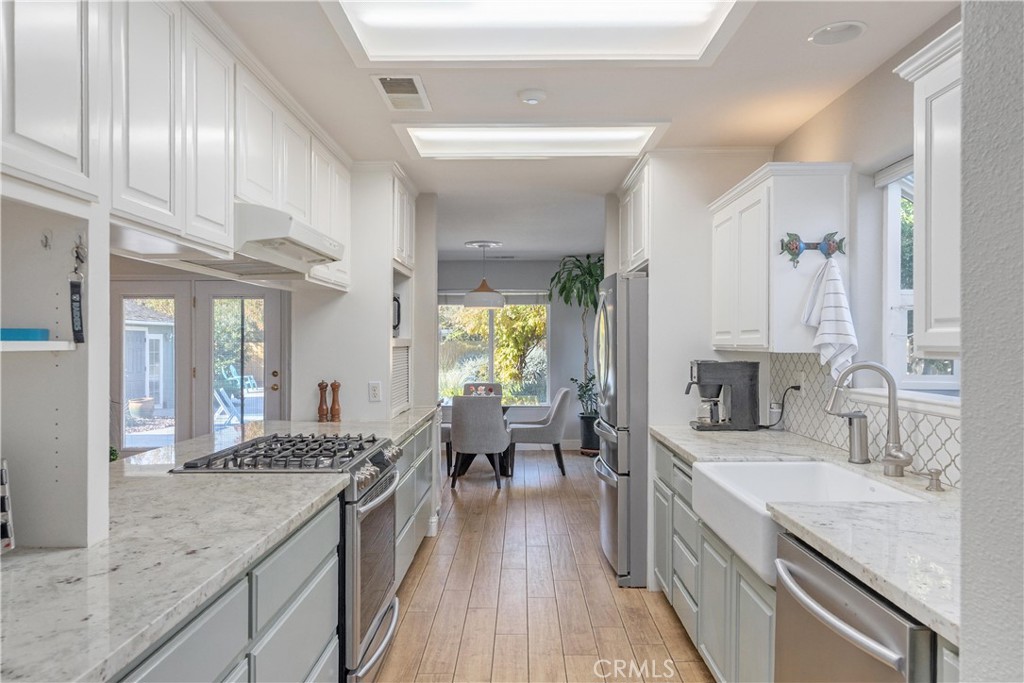 Galley kitchen with white cabinets, stone counters, a farmhouse sink, and a dining area by the window.