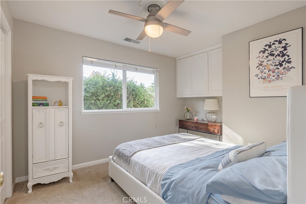Furnished bedroom with pale blue bedding, a ceiling fan, and a large window overlooking greenery.