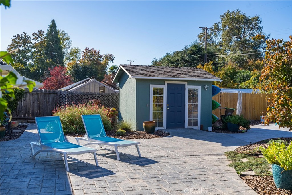 Backyard patio with a blue-gray shed, two turquoise lounge chairs, and autumn foliage.