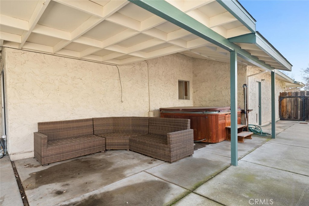 Covered patio with a wicker sectional and wooden hot tub beside the house.