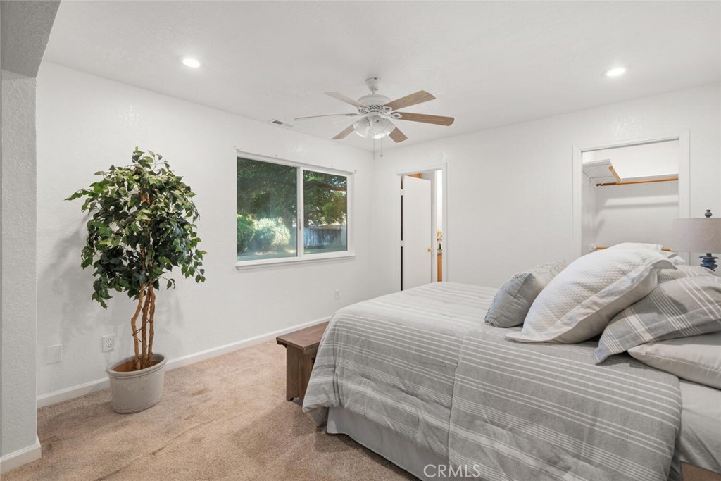 Furnished bedroom with a gray striped bed, ceiling fan, and window overlooking greenery.