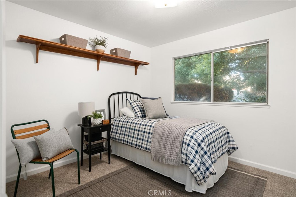 Bedroom with a plaid-covered single bed, large window, and wooden wall shelf.