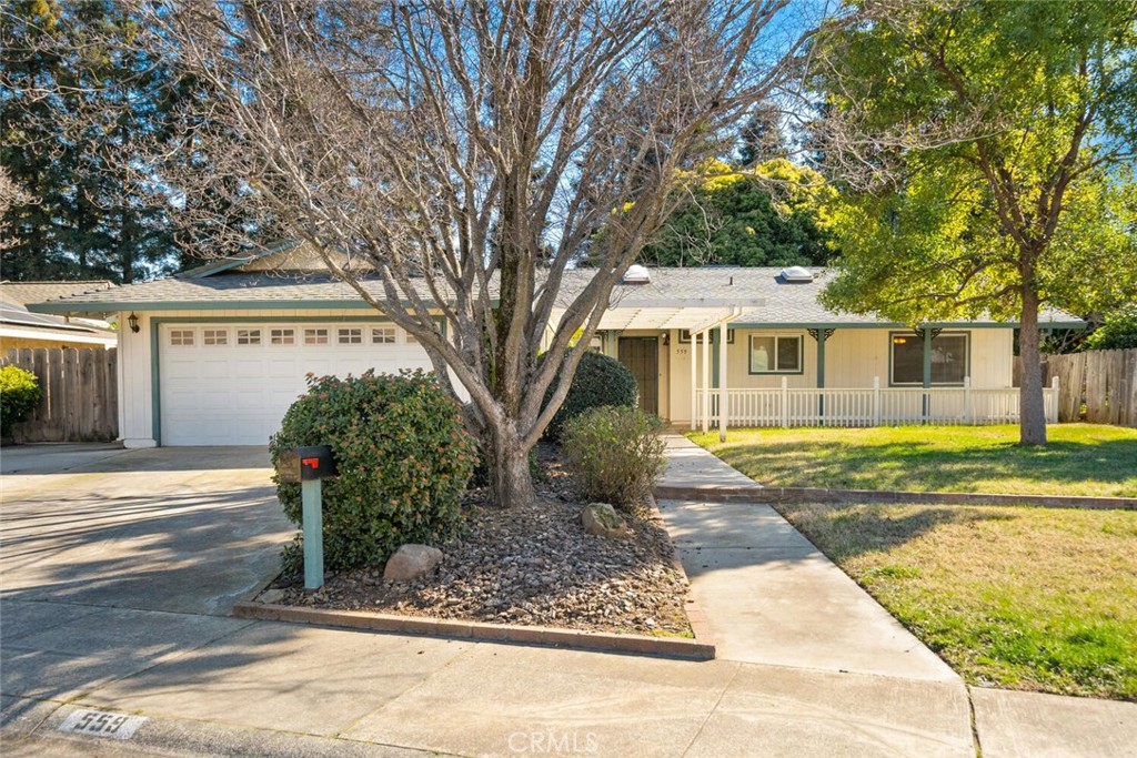 Single-story home with a white double garage, covered porch, and mature trees in front.