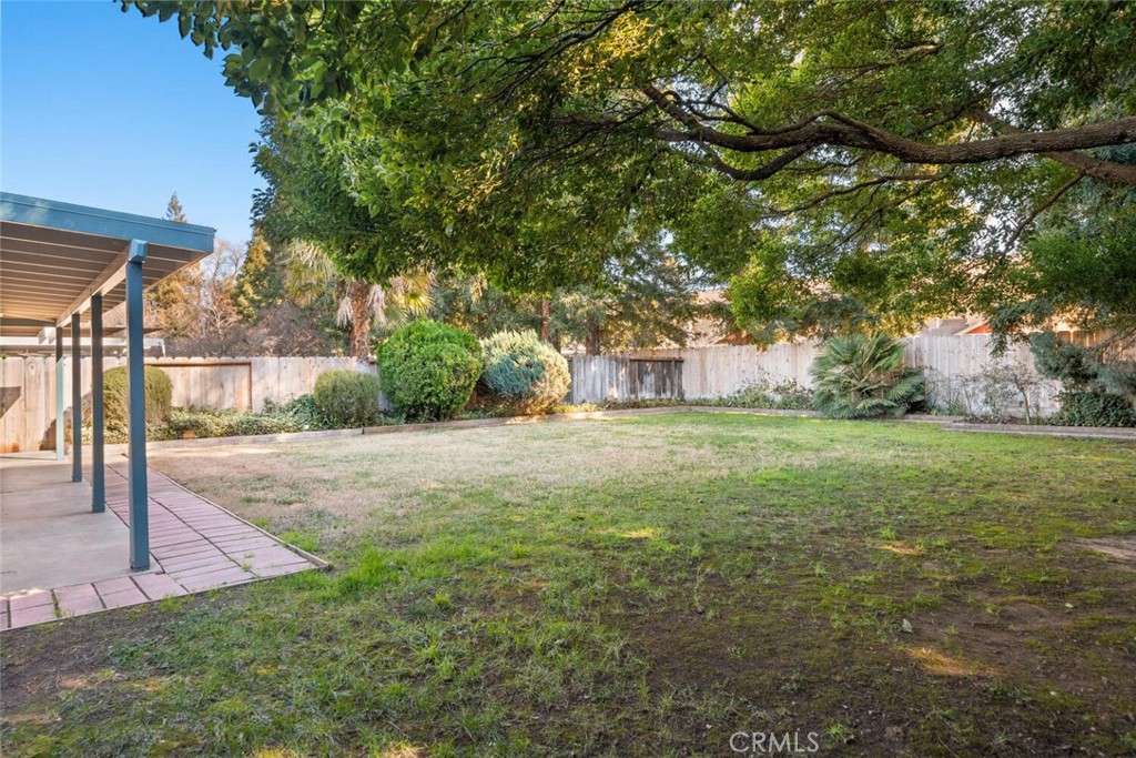 Fenced backyard with a broad lawn, mature shade tree, and covered patio.