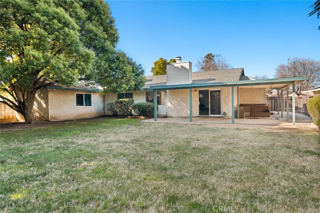 Rear of a single-story house with a covered patio, sliding doors, and a large grassy backyard.