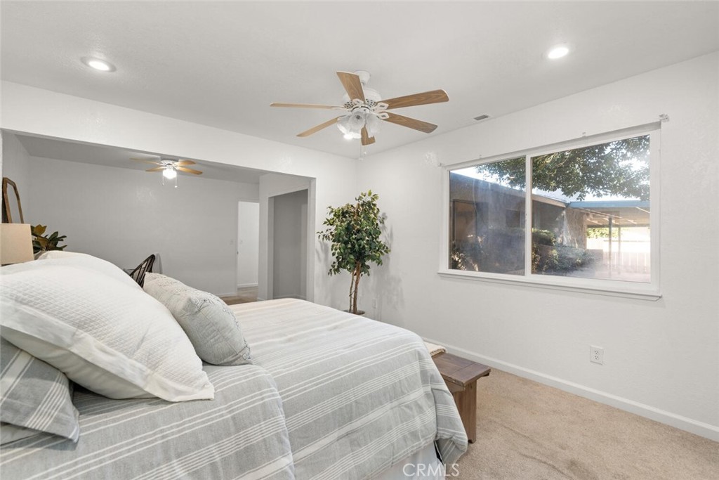 Staged bedroom with striped bedding, two ceiling fans, and a wide window overlooking the yard.