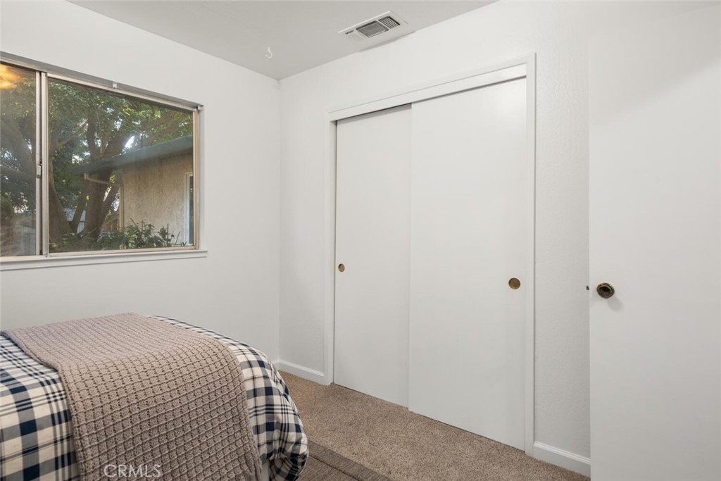 Bedroom with a sliding-door closet, tree-view window, and corner of a plaid-covered bed.