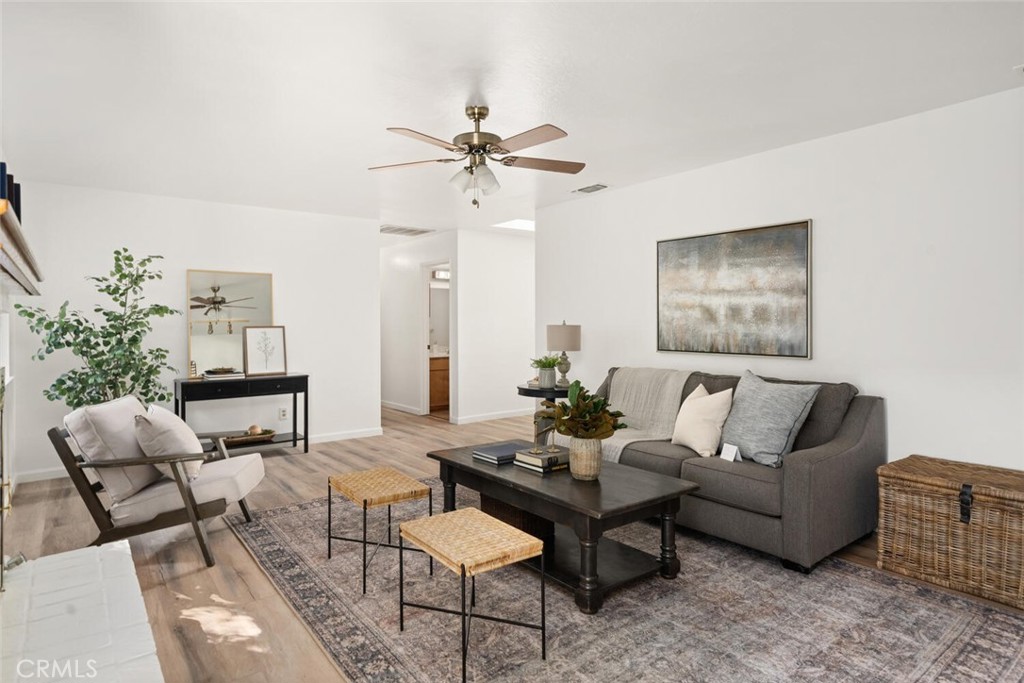 Staged living room with gray sofa, dark coffee table, ceiling fan, and wood-look flooring.