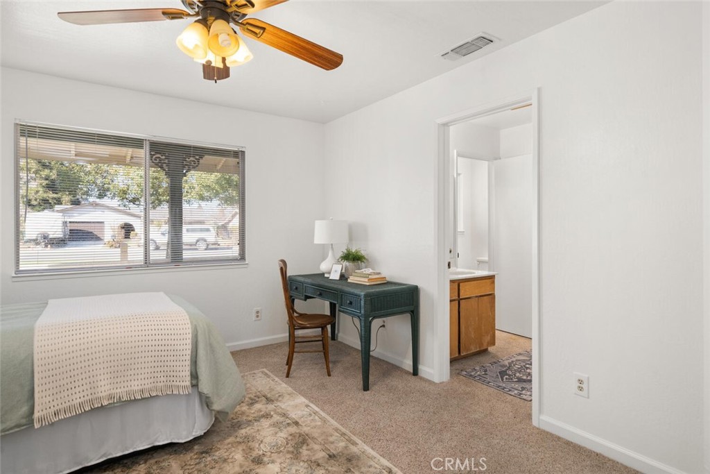 Bedroom with a ceiling fan, desk, and doorway to a bathroom