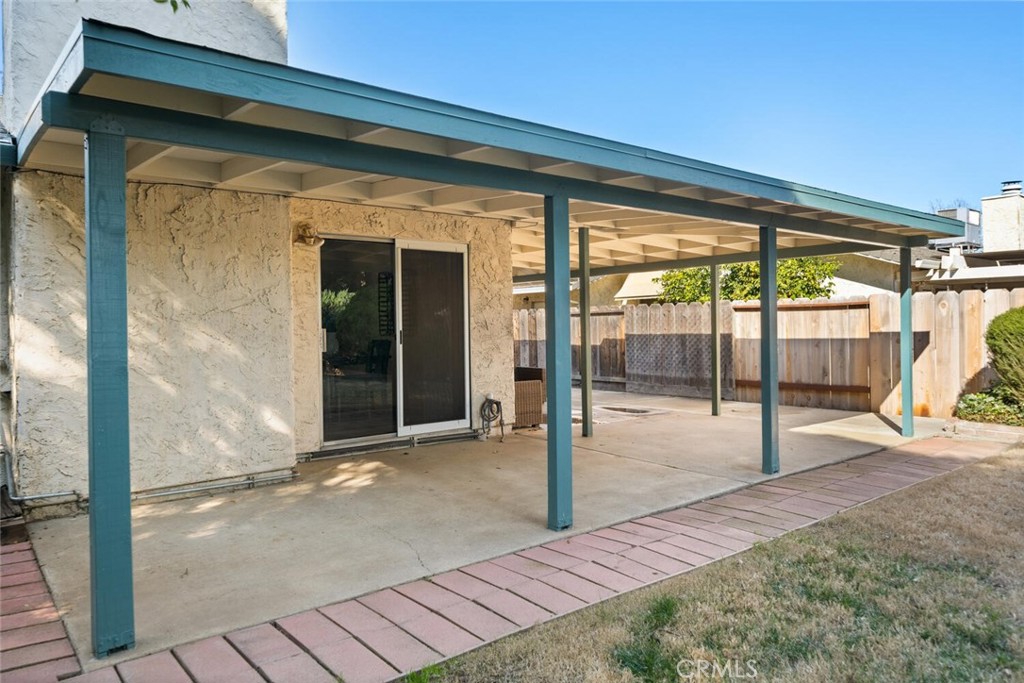 Covered concrete patio with teal support posts beside a fenced backyard.