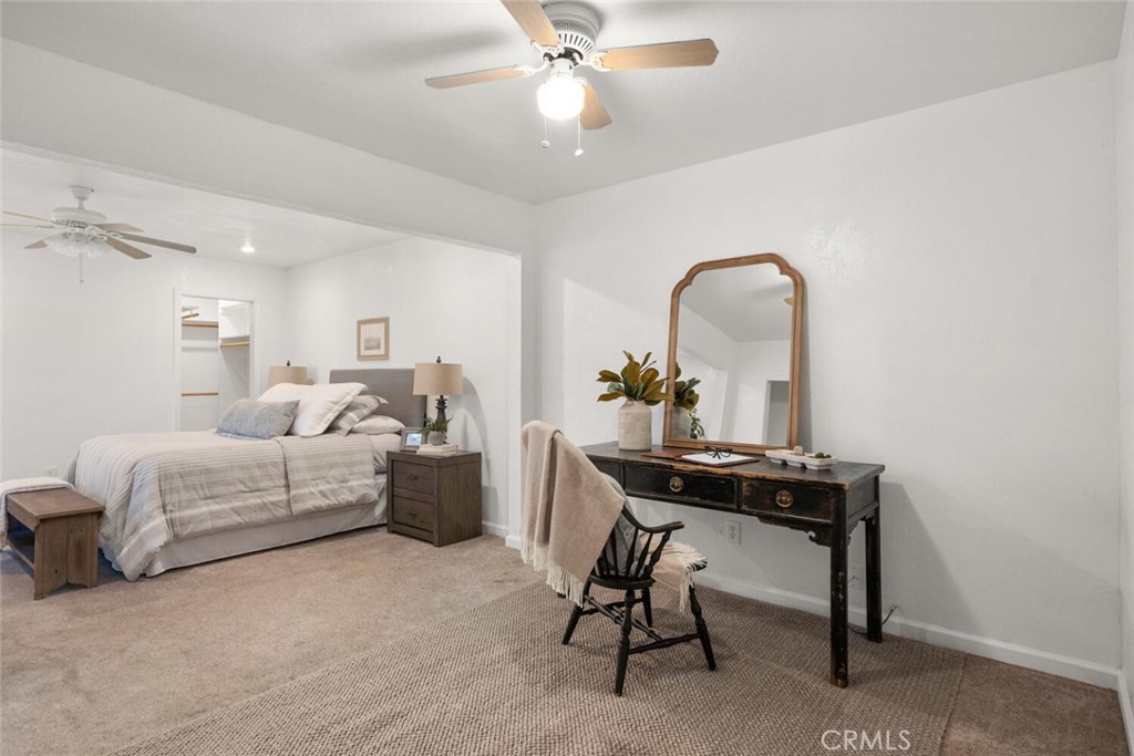 Staged bedroom with a bed and dark wood desk topped by an arched mirror.