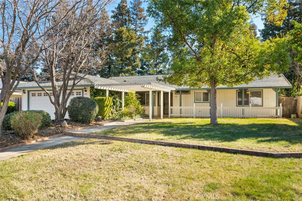Single-story home with a covered porch and attached garage, framed by mature trees and a broad lawn.