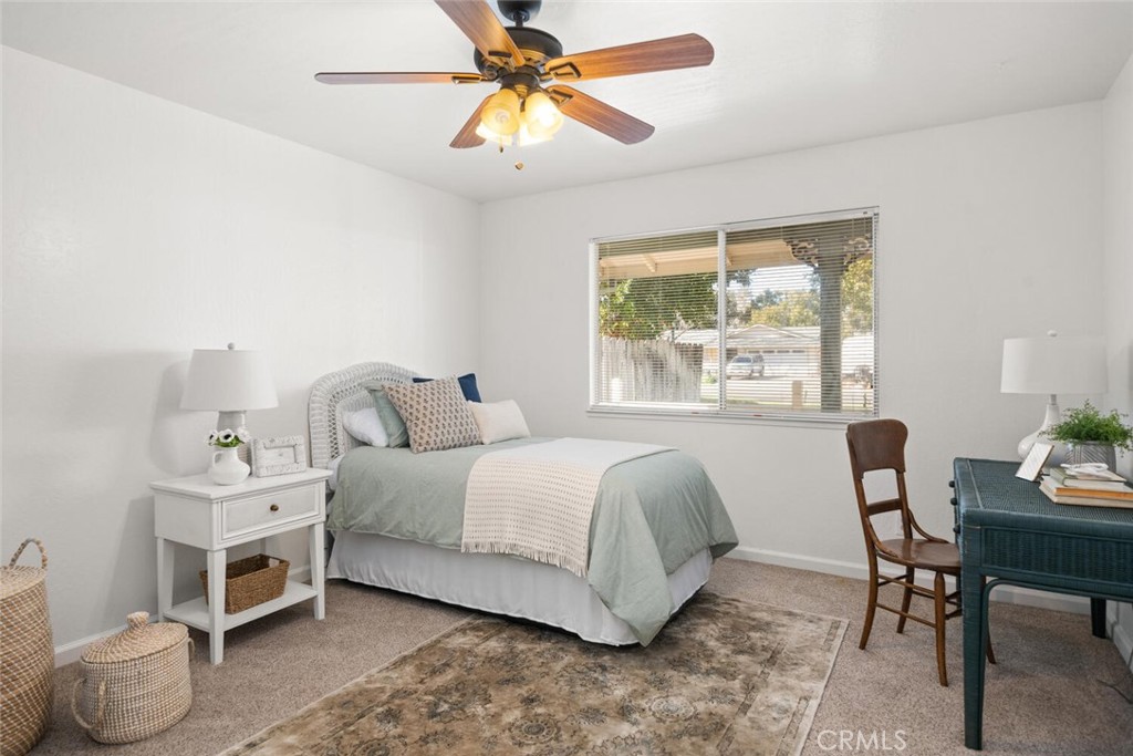 Staged bedroom with a pale green bed, wooden-blade ceiling fan, window blinds, and patterned rug.