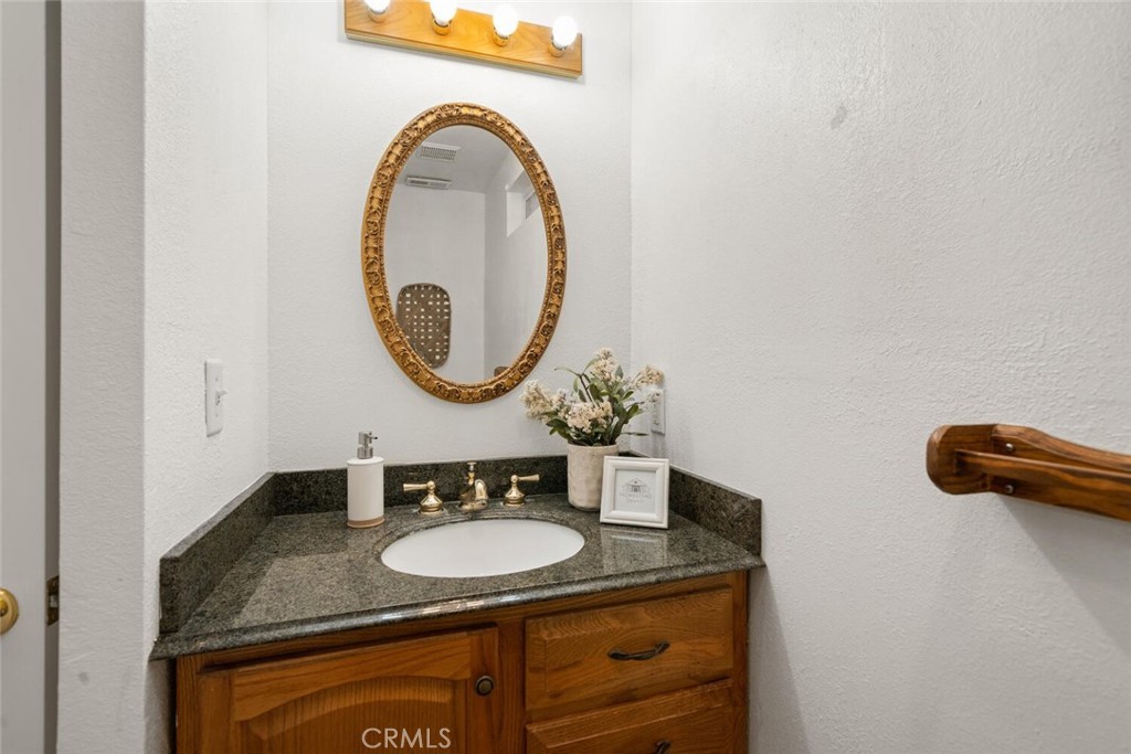 Bathroom vanity with dark granite counter, wood cabinet, brass fixtures, and an ornate oval mirror.