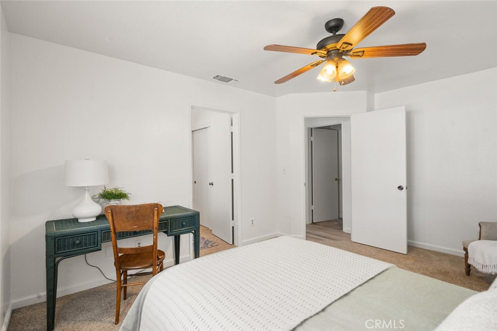 Furnished bedroom with a teal desk, wooden chair, and ceiling fan with lights.