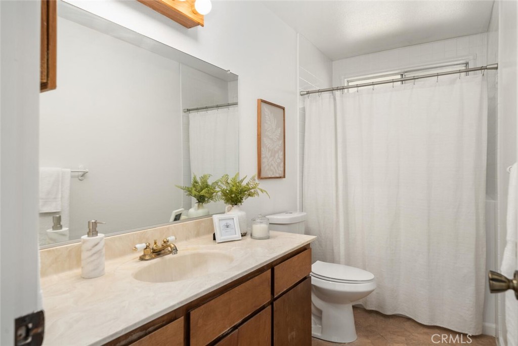 Bathroom with a wood vanity, pale stone counter, large mirror, and white shower curtain.