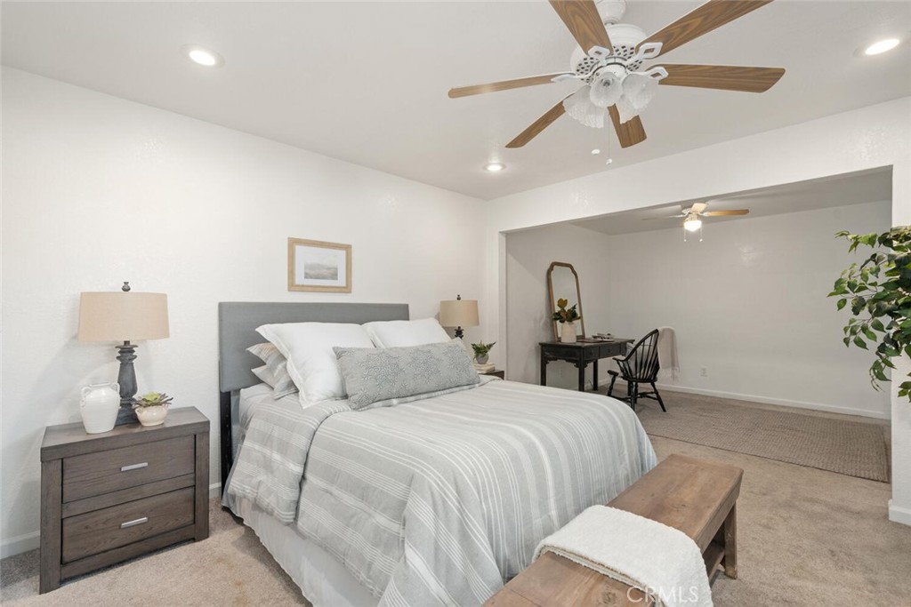 Staged bedroom with striped bedding, a wood bench, and an adjoining desk area.