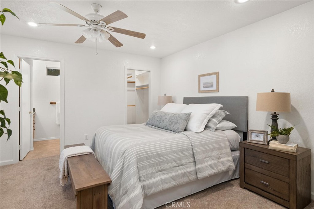 Staged bedroom with striped bedding, a gray headboard, ceiling fan, and open bathroom doorway.