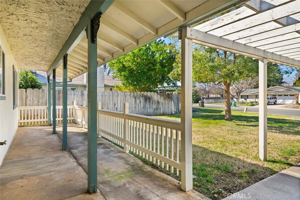 Covered concrete patio with white railings and a pergola overlooking a grassy yard.