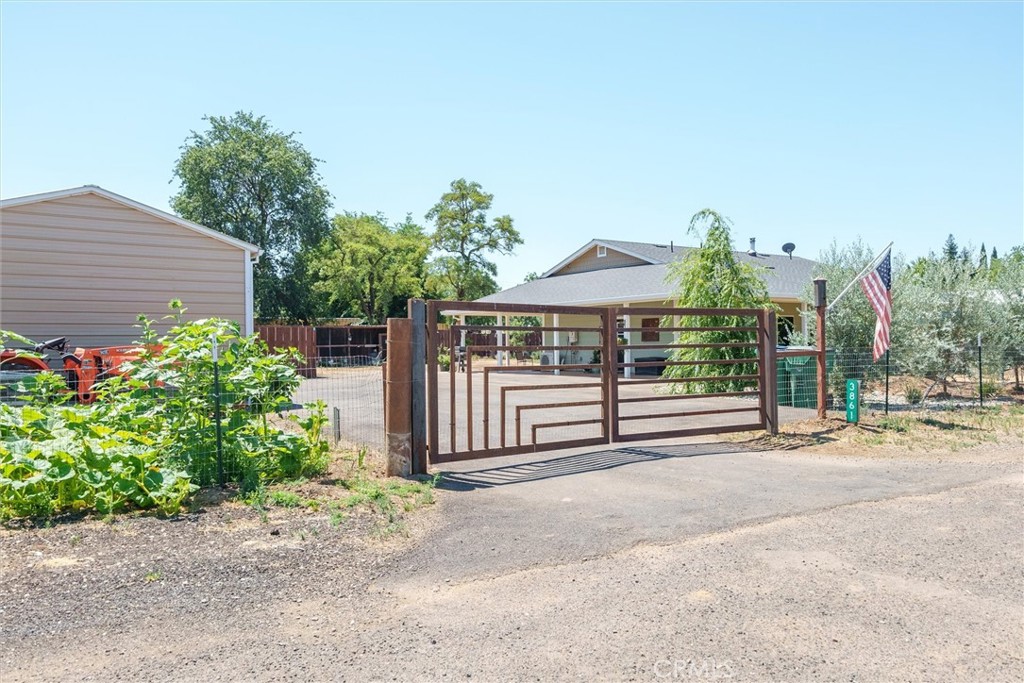 House behind a brown metal driveway gate, with a fenced yard and an American flag.