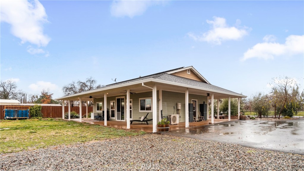 Single-story house with a broad covered patio, gravel foreground, and wet driveway.