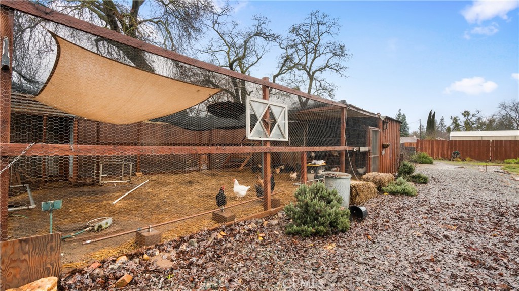 Fenced chicken run with chickens beneath a tan shade canopy beside a gravel yard.