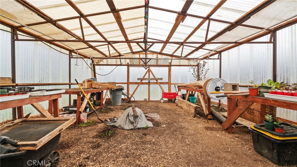 Greenhouse interior with wooden workbenches, potted plants, and translucent walls and roof.