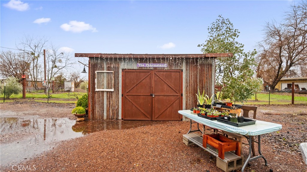 Rustic garden shed with red barn doors and a nearby table of potted plants.