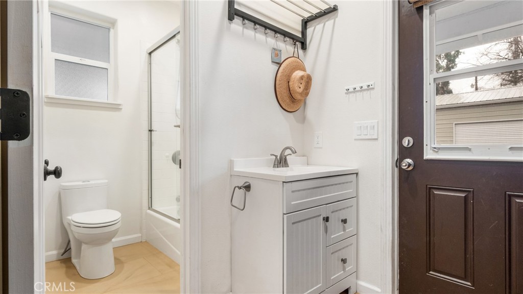 Bathroom with a glass shower, white toilet, gray vanity, and dark brown door.